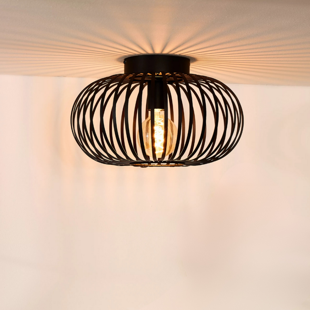 Zwarte metalen plafondlamp met open draadkap en warm lichtpatroon op plafond