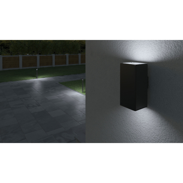 Grijze up down wandlamp verlicht muur en betegeld terras in de avond