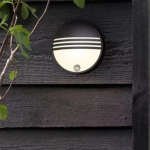 Zwarte ronde wandlamp met bewegingssensor op houten buitenmuur