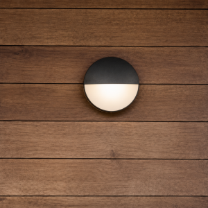 Ronde grijze wandlamp met diffuus warm licht tegen houten gevel