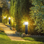 Grijze tuinsokkel met warm wit licht langs tuinpad tussen groene hagen
