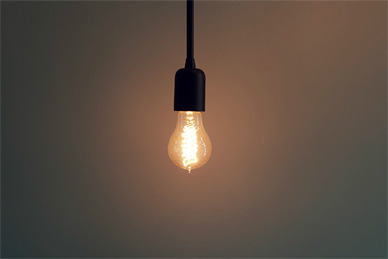 Hangende gloeilamp met warm licht tegen neutrale muur
