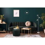 Witte vloerlamp met drie verstelbare spots naast donkergroene fluwelen bank.