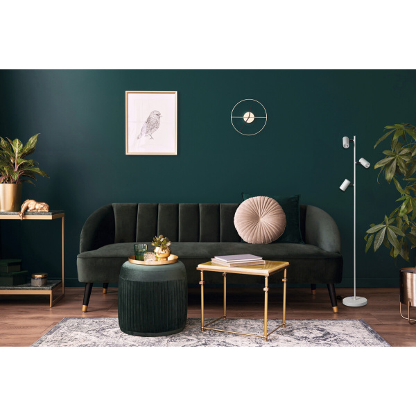 Witte vloerlamp met drie verstelbare spots naast donkergroene fluwelen bank.