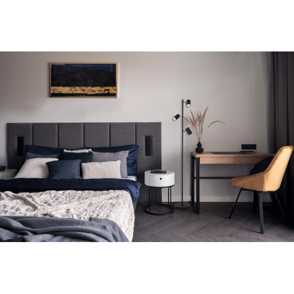 Zwarte vloerlamp met drie verstelbare spots naast bed en houten bureau.