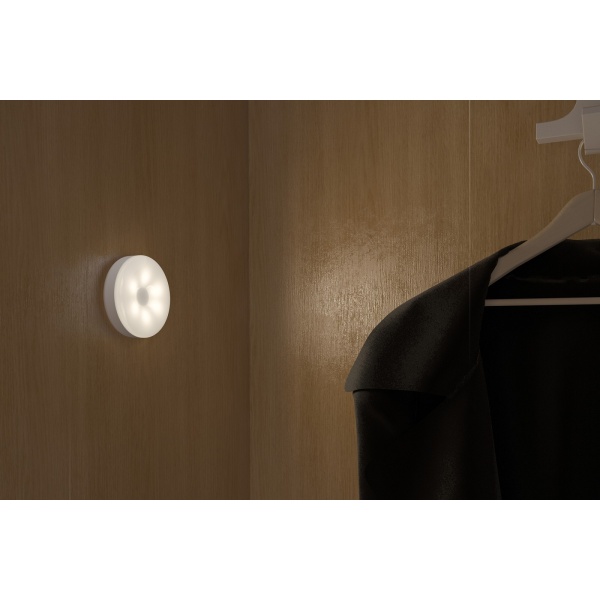 Ronde witte pucklight met warm licht in houten kast naast kledinghanger.