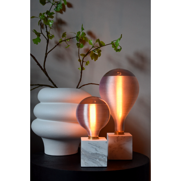 Twee glazen tafellampen met wit marmeren voet naast witte vaas met tak.