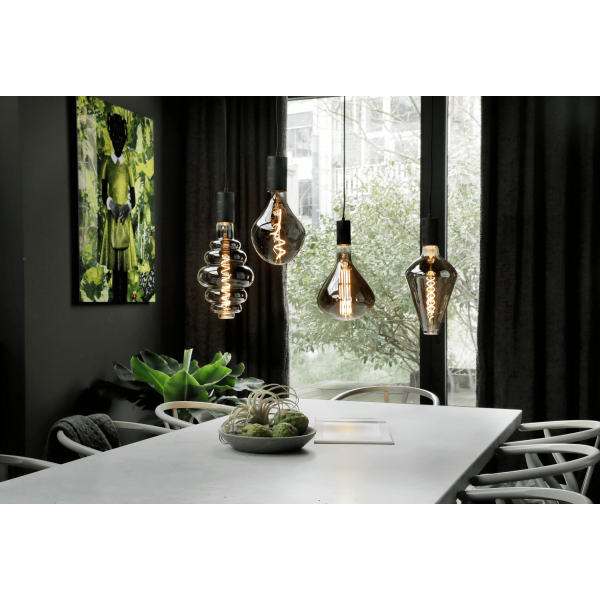 Vier hangende LED filamentlampen boven een eettafel met planten