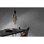 Grote glaslamp met spiraal filament boven donkere eettafel tegen grijze muur