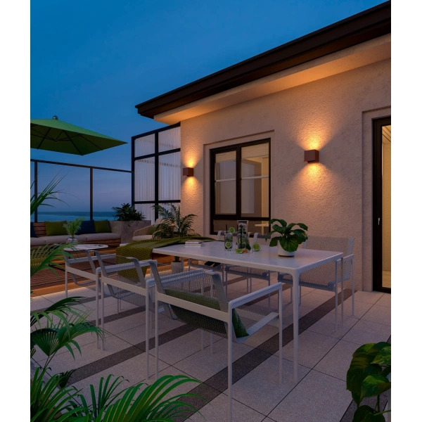 Wandlampen met warm licht aan gevel boven buitenterras met tuinset