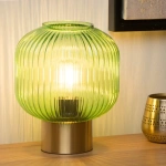 Groene glazen tafellamp met messing voet op houten tafel in warme setting