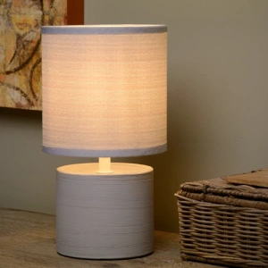 Grijze ronde tafellamp met stoffen kap op houten tafel naast rieten mand