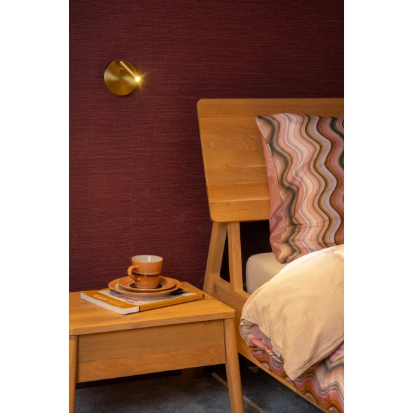 Gouden wandlamp naast houten bed met nachtkastje en kleurrijk kussen