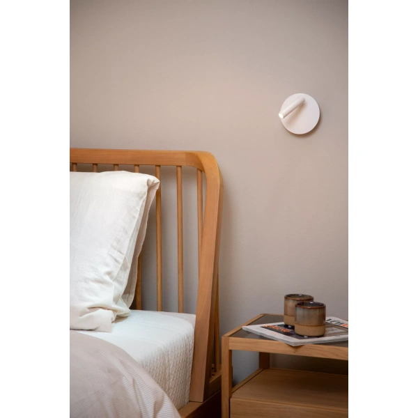 Witte ronde bedlamp aan muur naast houten bed en nachtkastje