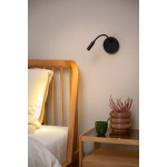 Zwarte verstelbare bedlamp aan muur naast houten bed en nachtkastje.