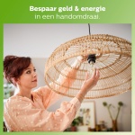 Vrouw draait LED lamp in rieten hanglamp boven eettafel