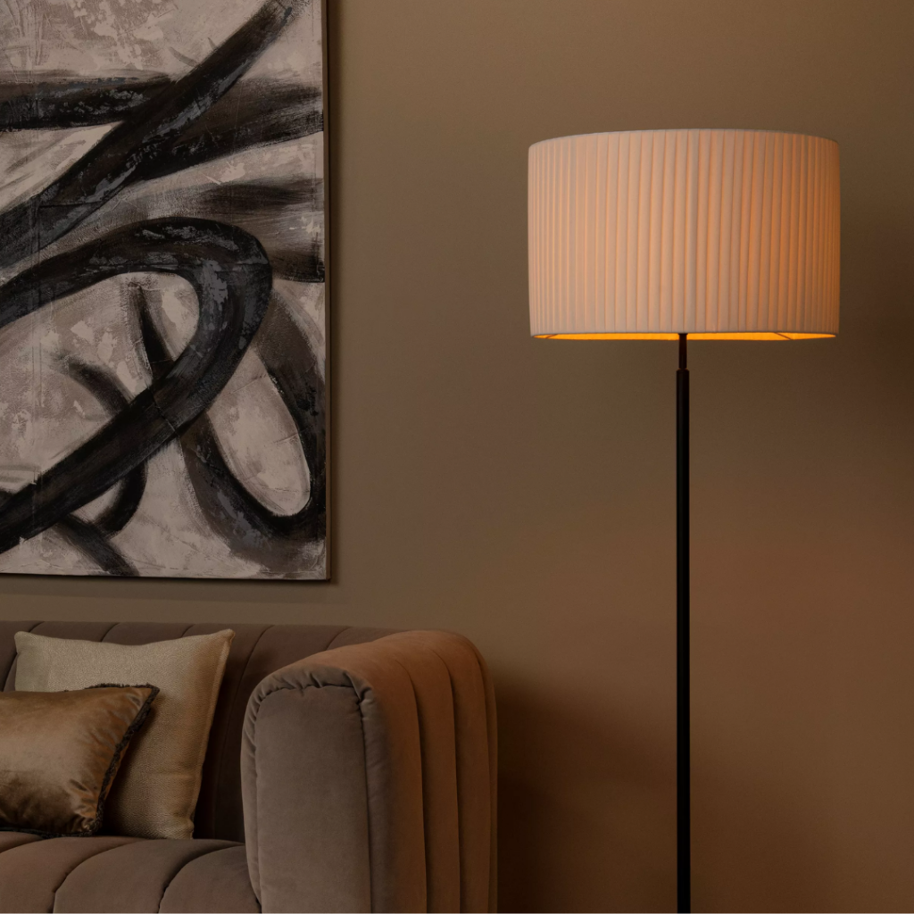 Witte ronde vloerlamp met geplooide kap naast beige bank in woonkamer