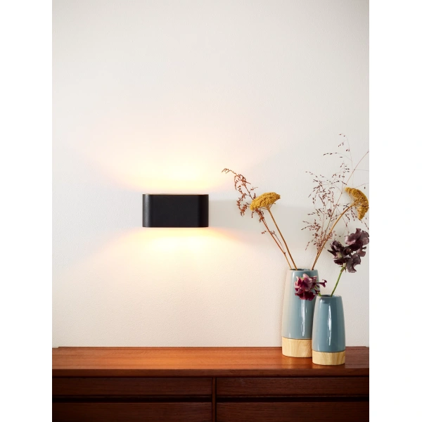 Zwarte ovale wandlamp met licht omhoog en omlaag boven houten dressoir