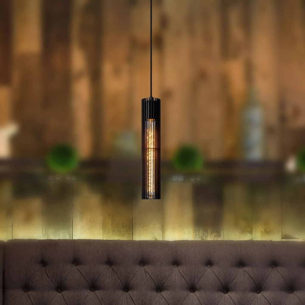 Zwarte cilindervormige hanglamp met warm licht boven een gestoffeerde bank