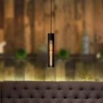 Zwarte cilindervormige hanglamp met warm licht boven een gestoffeerde bank