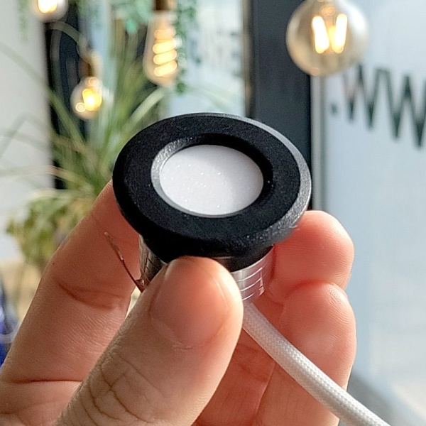 Kleine zwarte inbouwspot met ronde rand vastgehouden in hand