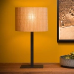 Bamboe tafellamp met zwarte metalen voet op houten tafel tegen gele muur