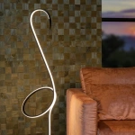 Vloerlamp zwart met gebogen LED lichtlijn naast bruine bank