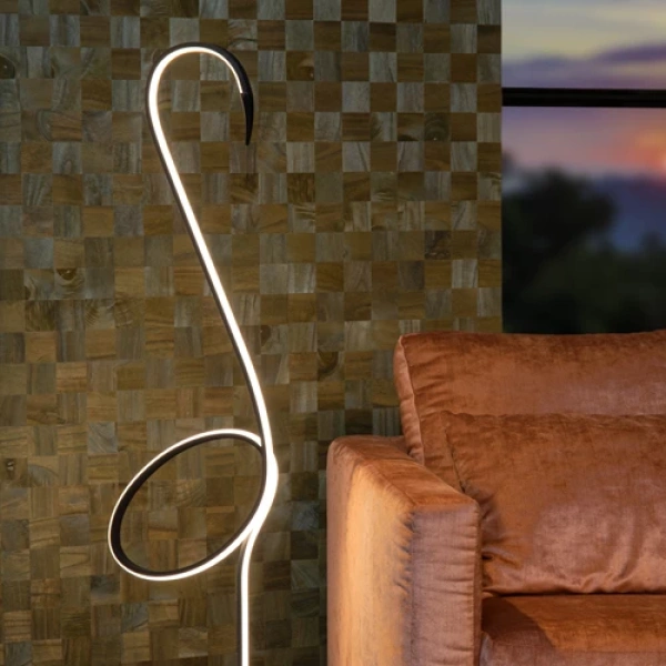 Vloerlamp zwart met gebogen LED lichtlijn naast bruine bank