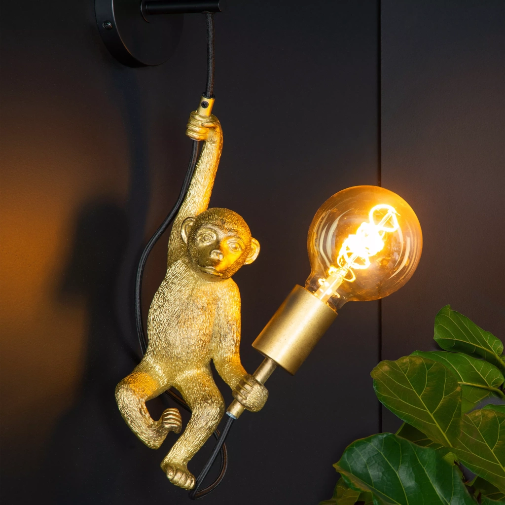 Wandlamp in goudkleurige apenvorm met zichtbare gloeilamp aan zwarte muur