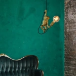 Gouden hanglamp in apenvorm met zichtbare gloeilamp boven groene muur en bank