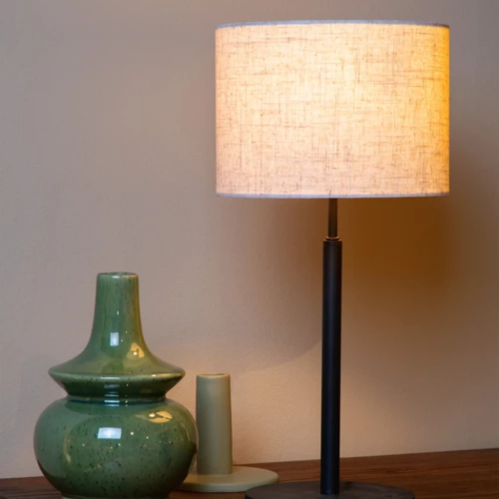 Beige Scandinavische tafellamp met stoffen kap op zwarte voet naast groene vaas