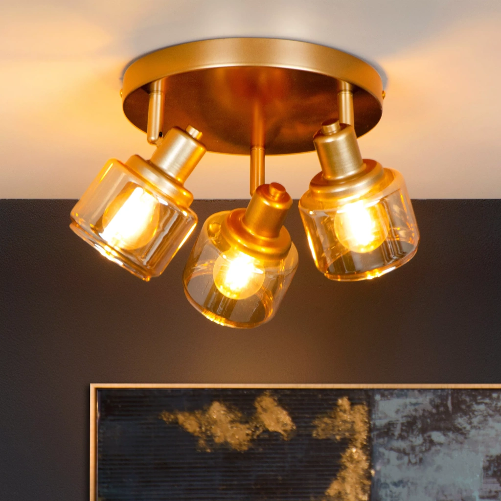 Gouden messing plafondspot met drie verstelbare lichtpunten en warm licht in woonkamer