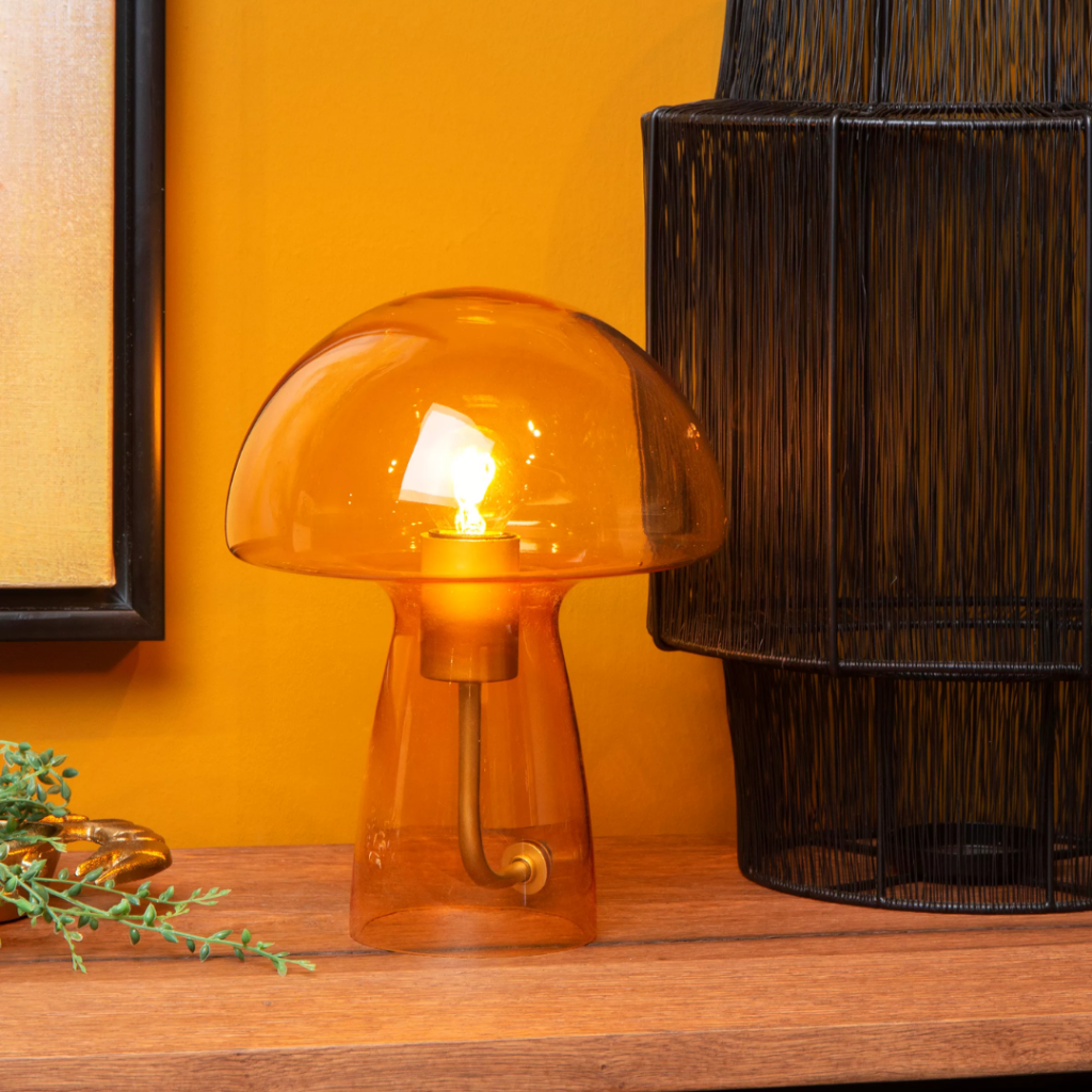 Oranje glazen paddenstoel tafellamp met warme gloed op houten tafel