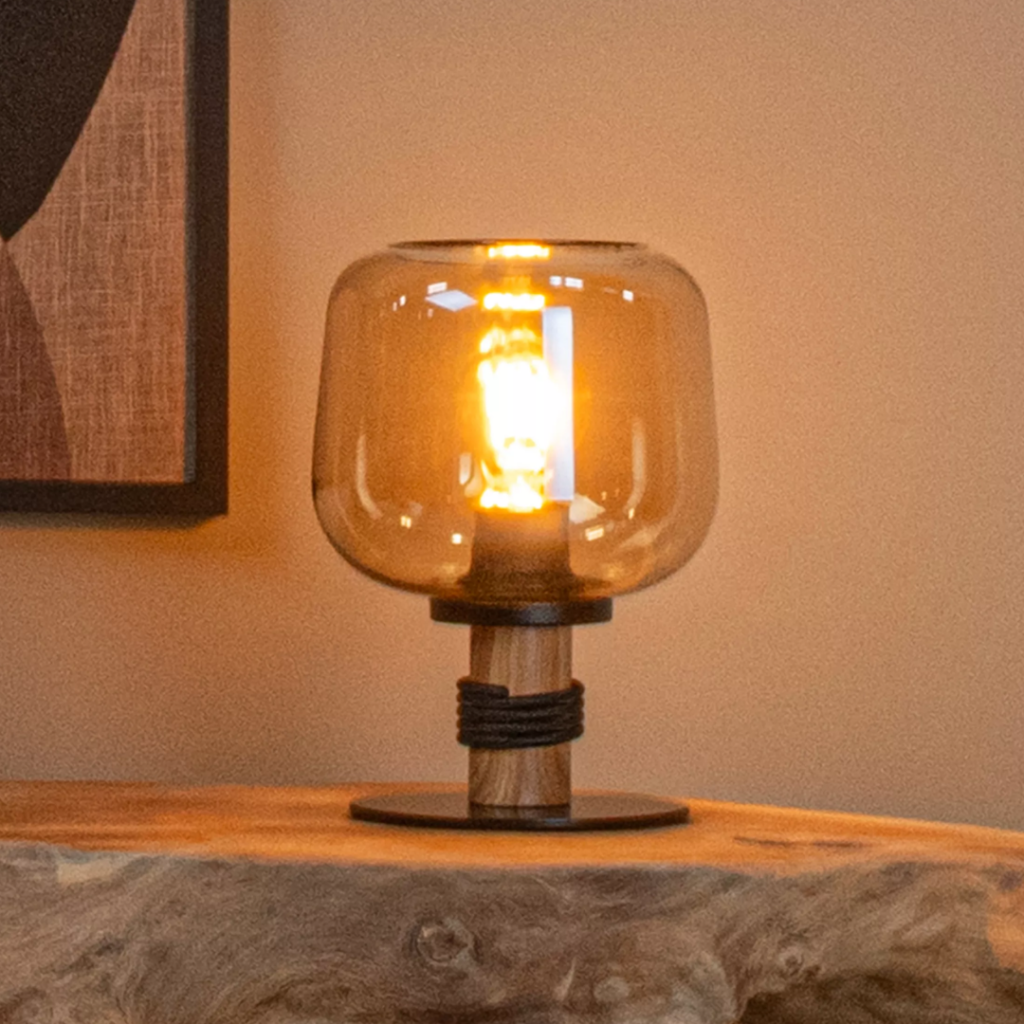 Amberkleurige glazen tafellamp met houten voet op houten tafel in warm interieur