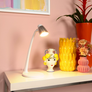 Witte en zilveren bureaulamp met gebogen arm verlicht plank met kleurrijke decoratie