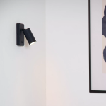 Zwarte moderne wandlamp met geribbelde kap verlicht witte muur in interieur