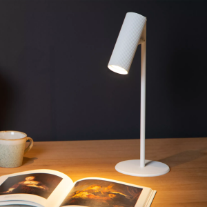 Witte moderne bureaulamp met geribbelde kap verlicht een houten werkblad met boek