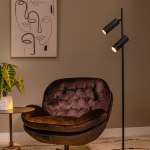 Zwarte moderne vloerlamp met twee spots naast fauteuil in warme woonkamer