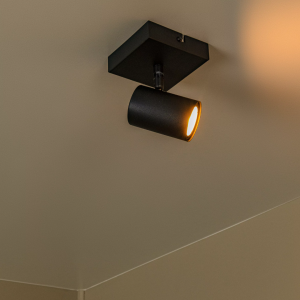 Zwarte moderne spotlamp met één lichtpunt aan plafond in warme verlichting