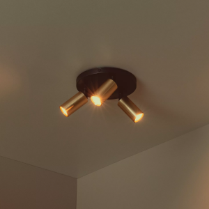 Gouden messing plafondspot met drie verstelbare lichtpunten in warme verlichting