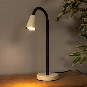 Beige tafellamp met zwarte gebogen steel op houten tafel naast plant