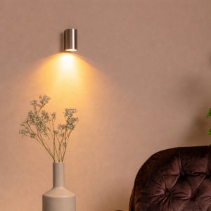 Moderne grijze metalen wandlamp met warm downlight boven fauteuil en vaas