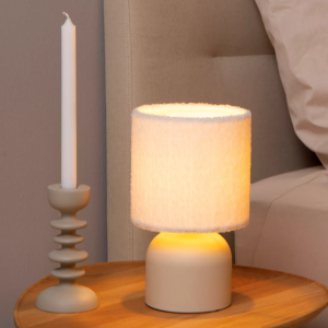 Beige tafellamp met zachte stoffen kap op houten nachtkastje naast bed