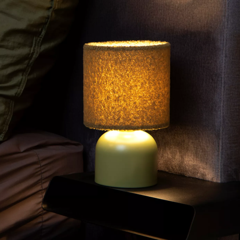 Groene tafellamp met stoffen kap verspreidt warm licht op nachtkastje