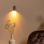 Moderne koffiebruine wandlamp met warm downlight boven fauteuil en vaas