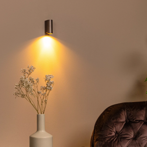 Moderne koffiebruine wandlamp met warm downlight boven fauteuil en vaas