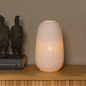 Witte keramische tafellamp met geperforeerd patroon verspreidt warm licht op houten kast