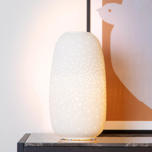 Witte keramische tafellamp met subtiel lichtpatroon op donkere tafel