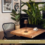 Oplaadbare roestkleurige tafellamp met warm licht op houten tafel in cafésetting