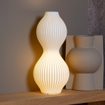 Witte ribbelvormige tafellamp van keramiek met warm licht op houten plank